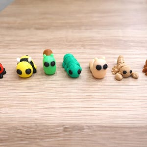 May include: A collection of colorful, handcrafted insect figurines. The set includes a red ladybug with black spots, a yellow bee, a green caterpillar, and a brown spider. Each figure is detailed and unique, perfect for collectors.