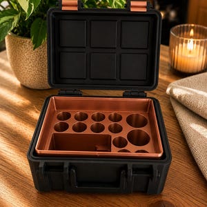 May include: Black and copper-colored storage case, open to reveal an interior with various compartments and circular holders. The case has a handle and latches. The interior is a contrasting copper color. The case is on a wooden surface.