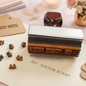 May include: A DIY custom stamp with interchangeable letter blocks. The stamp has a wooden base and a clear plastic top. The words "DIY CUSTOM STAMP" are printed on the paper. Small wooden blocks with letters are scattered around the stamp.