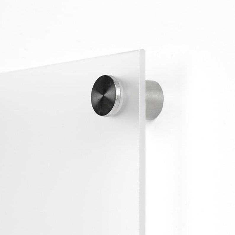 May include: A close-up of a white acrylic print with a silver hanging hardware. The hardware has a black metal cap.