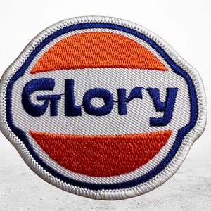 Peut inclure: Écusson brodé blanc, bleu et orange avec le mot "Glory" en lettres bleues.