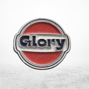 Può includere: Uno spillo circolare rosso, bianco e blu con la parola "Glory" in lettere bianche su una fascia bianca.