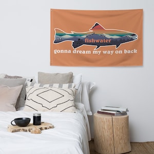 Op de afbeelding: Een perzikkleurig wandkleed met een silhouet van een vis tegen een zonsondergangachtergrond. De tekst "fishwater" staat in het midden van de vis en de tekst "gonna dream my way on back" staat onder de vis.