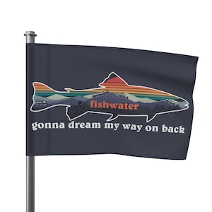 Puede incluir: Una bandera azul marino con una silueta de una trucha con una puesta de sol y una escena de montaña dentro del pez. El texto "fishwater" está dentro del pez y el texto "gonna dream my way on back" está debajo del pez.