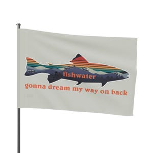 Op de afbeelding: Een witte vlag met een kleurrijk silhouet van een vis. De vis is gevuld met een berglandschap en een zonsondergang. De tekst "fishwater gonna dream my way on back" staat onder de vis.