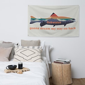 Op de afbeelding: Een beige wandkleed met een kleurrijk silhouet van een vis en de tekst "fishwater gonna dream my way on back".