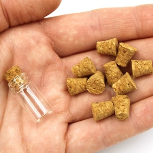 May include: A small glass bottle with a cork stopper and a pile of cork stoppers in a hand.
