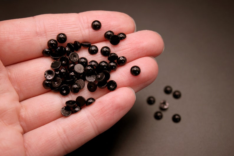 May include: A pile of black plastic buttons in a hand. The buttons are round and have a flat back.