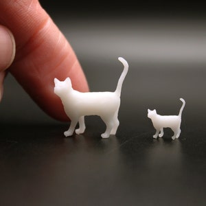 Puede incluir: Dos figuritas de gato blancas impresas en 3D. El gato m&aacute;s grande est&aacute; de pie con la cola levantada. El gato m&aacute;s peque&ntilde;o est&aacute; sentado con la cola enroscada.