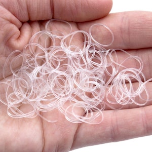 May include: A large pile of clear rubber hair ties in a person's hand.