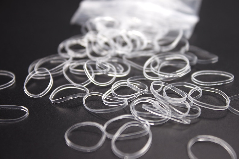 May include: A pile of clear rubber hair ties on a black surface.
