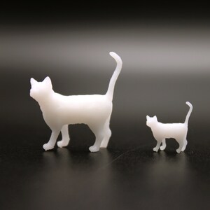 Puede incluir: Dos figuritas de gatos de pl&aacute;stico blanco, una m&aacute;s grande que la otra. El gato m&aacute;s grande est&aacute; de pie con la cola levantada, mientras que el gato m&aacute;s peque&ntilde;o est&aacute; sentado con la cola enroscada alrededor de su cuerpo.