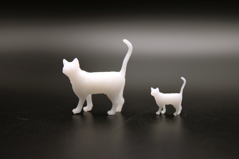 Puede incluir: Dos figuritas de gatos de pl&aacute;stico blanco, una m&aacute;s grande que la otra. El gato m&aacute;s grande est&aacute; de pie con la cola levantada, mientras que el gato m&aacute;s peque&ntilde;o est&aacute; sentado con la cola enroscada alrededor de su cuerpo.