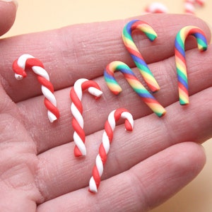 May include: A collection of six miniature candy canes, two red and white and four rainbow striped, in a person's hand.