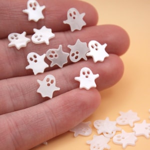 May include: A collection of small, white ghost-shaped embellishments. Each ghost has a simple, rounded form with two eye holes and a mouth. The ghosts are scattered, suggesting a craft or decorative theme, perfect for Halloween or spooky projects.