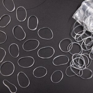 May include: A clear plastic bag filled with clear rubber hair ties, with some hair ties scattered on a black surface.