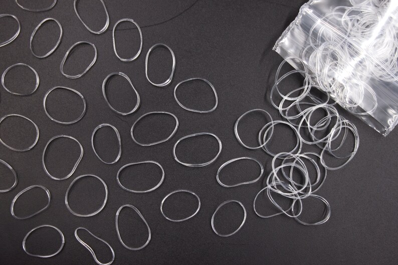 May include: A clear plastic bag filled with clear rubber hair ties, with some hair ties scattered on a black surface.