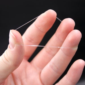 May include: A close-up of a hand holding a thin, clear elastic string.