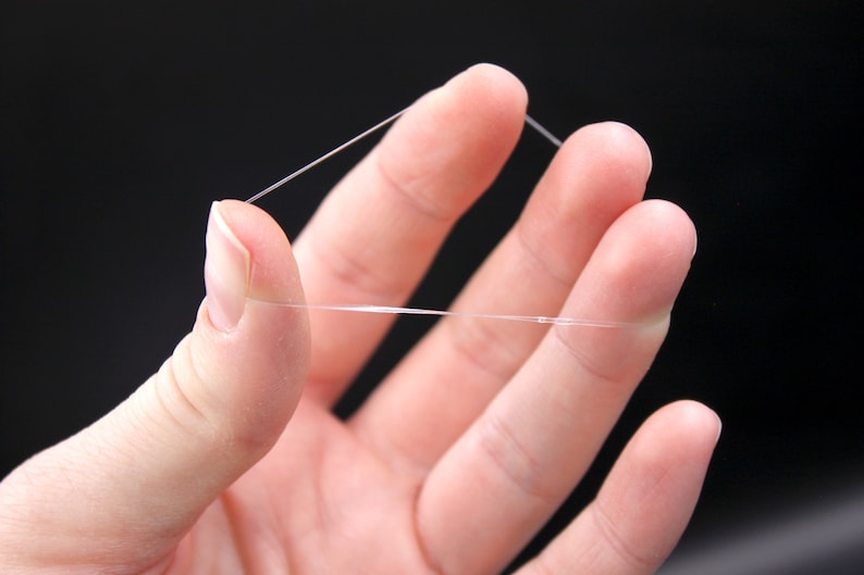 May include: A close-up of a hand holding a thin, clear elastic string.