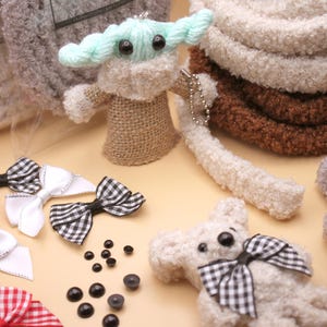 May include: A collection of handmade plush toys, including a green and white Baby Yoda, a gray bear with a red and white checkered bow, and a white bear with a black and white checkered bow. There are also several black plastic eyes and white, red, and black checkered bows.