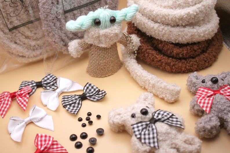 May include: A collection of handmade plush toys, including a green and white Baby Yoda, a gray bear with a red and white checkered bow, and a white bear with a black and white checkered bow. There are also several black plastic eyes and white, red, and black checkered bows.