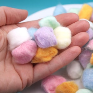 May include: A hand holding a variety of pastel colored cotton balls. The cotton balls are soft and fluffy, and they are perfect for crafts or cleaning.