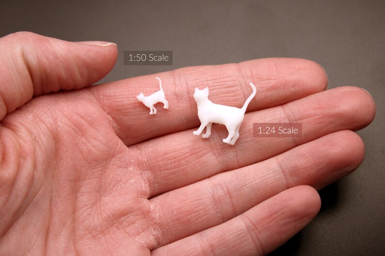 Puede incluir: Dos figuritas de gato de pl&aacute;stico blanco, una es m&aacute;s grande que la otra. El gato m&aacute;s grande est&aacute; etiquetado como "1:24 Scale" y el gato m&aacute;s peque&ntilde;o est&aacute; etiquetado como "1:50 Scale".