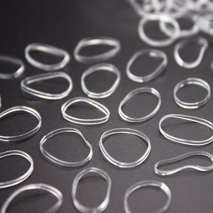 May include: A close-up of a group of clear rubber hair ties on a black surface. The hair ties are arranged in a pattern, with some overlapping.