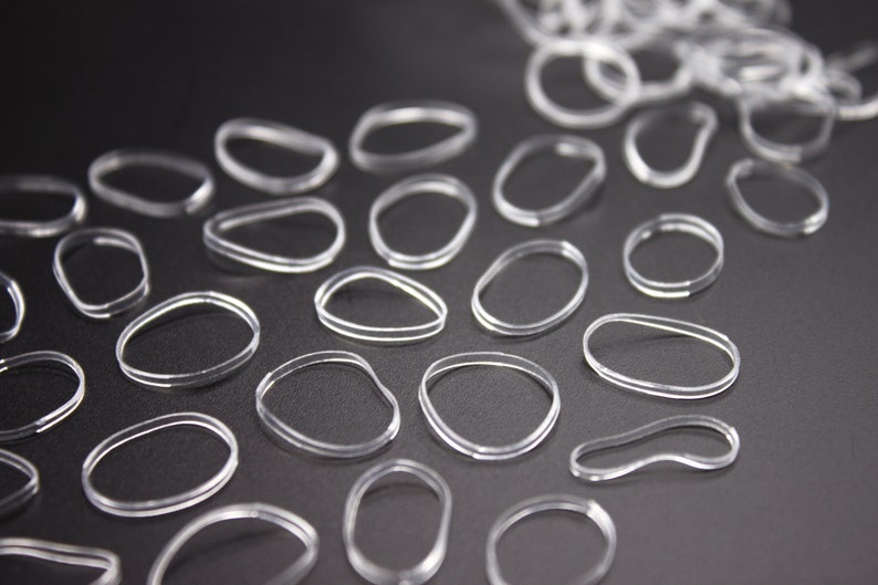 May include: A close-up of a group of clear rubber hair ties on a black surface. The hair ties are arranged in a pattern, with some overlapping.
