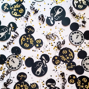 May include: Black and gold Mickey Mouse-shaped party decorations with a New Year's Eve theme. The decorations feature images of champagne bottles, clocks, and the text "Cheers" and "Happy New Year".