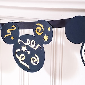 May include: Black and gold Mickey Mouse themed banner with a clock, champagne bottle, and confetti designs. The banner is made of black cardstock and features gold glitter accents.