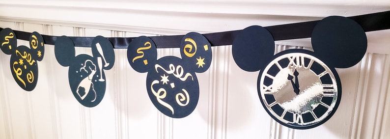 May include: Black and gold Mickey Mouse themed banner with a clock, champagne bottle, and confetti designs. The banner is made of black cardstock and features gold glitter accents.