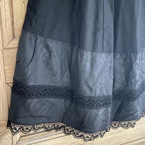 May include: Black skirt with a lace trim. The skirt has a tiered design with a smooth top layer and a textured bottom layer.