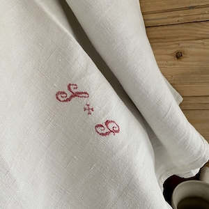 Op de afbeelding: Wit linnen tafelkleed met een rood geborduurd monogram "F & S" in het midden.