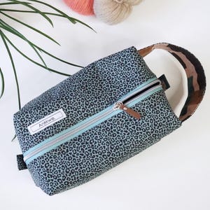 May include: A rectangular zippered pouch featuring a dark gray and black leopard print pattern. The bag includes a light blue zipper tape, a silver metal zipper pull with a brown leather tab, and a white rectangular label with the text AnMiwe.