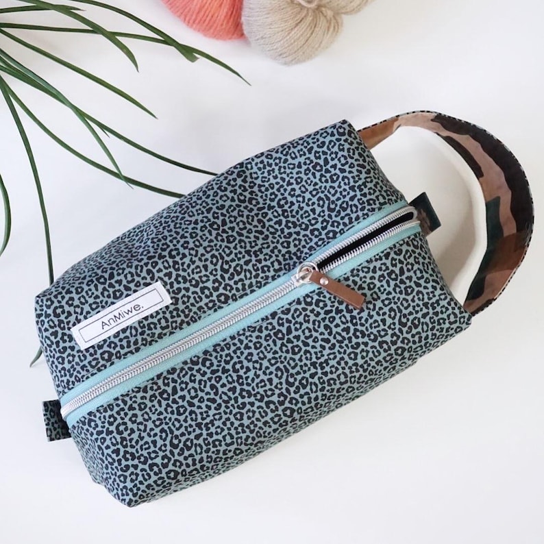 May include: A rectangular zippered pouch featuring a dark gray and black leopard print pattern. The bag includes a light blue zipper tape, a silver metal zipper pull with a brown leather tab, and a white rectangular label with the text AnMiwe.
