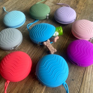 May include: Nine silicone pouches with zipper closures in various colours, including blue, green, purple, pink, and grey. Each pouch has a wavy pattern and a small loop for attaching a strap.