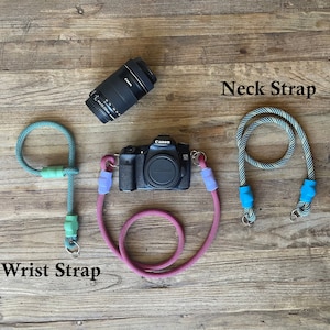 May include: A black Canon camera with a lens, a teal rope wrist strap with light green accents, and a black and white patterned rope neck strap with bright blue accents. The text Wrist Strap and Neck Strap are visible in the image.