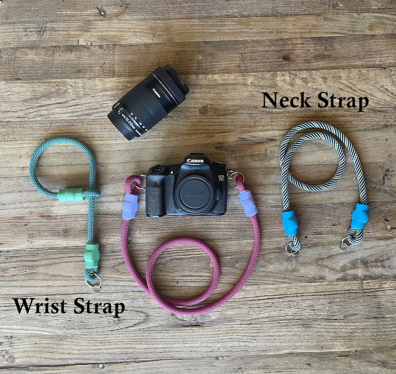 May include: A black Canon camera with a lens, a teal rope wrist strap with light green accents, and a black and white patterned rope neck strap with bright blue accents. The text Wrist Strap and Neck Strap are visible in the image.
