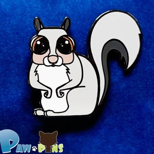 May include: White enamel pin of a cartoon sugar glider with large black eyes and a gray tail. The pin is on a blue background.  "Paw Pins" is written in the bottom left corner of the image. "Collectible pins that help animals in need" is written in the bottom center of the image.