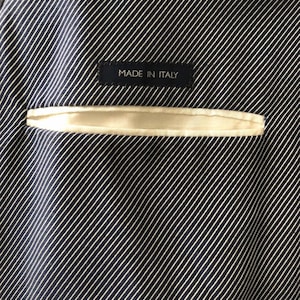 May include: Close-up of the interior lining of a dark navy blue blazer with white pinstripes. A small, rectangular label with the text "MADE IN ITALY" is sewn into the lining. A cream-colored pocket is visible.