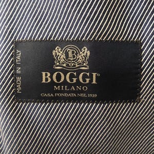 May include: Close-up of a navy blue and white striped fabric with a black label. The label reads "Boggi Milano" in gold lettering, with the text "Casa Fondata Nel 1939" below. The label also says "Made in Italy".