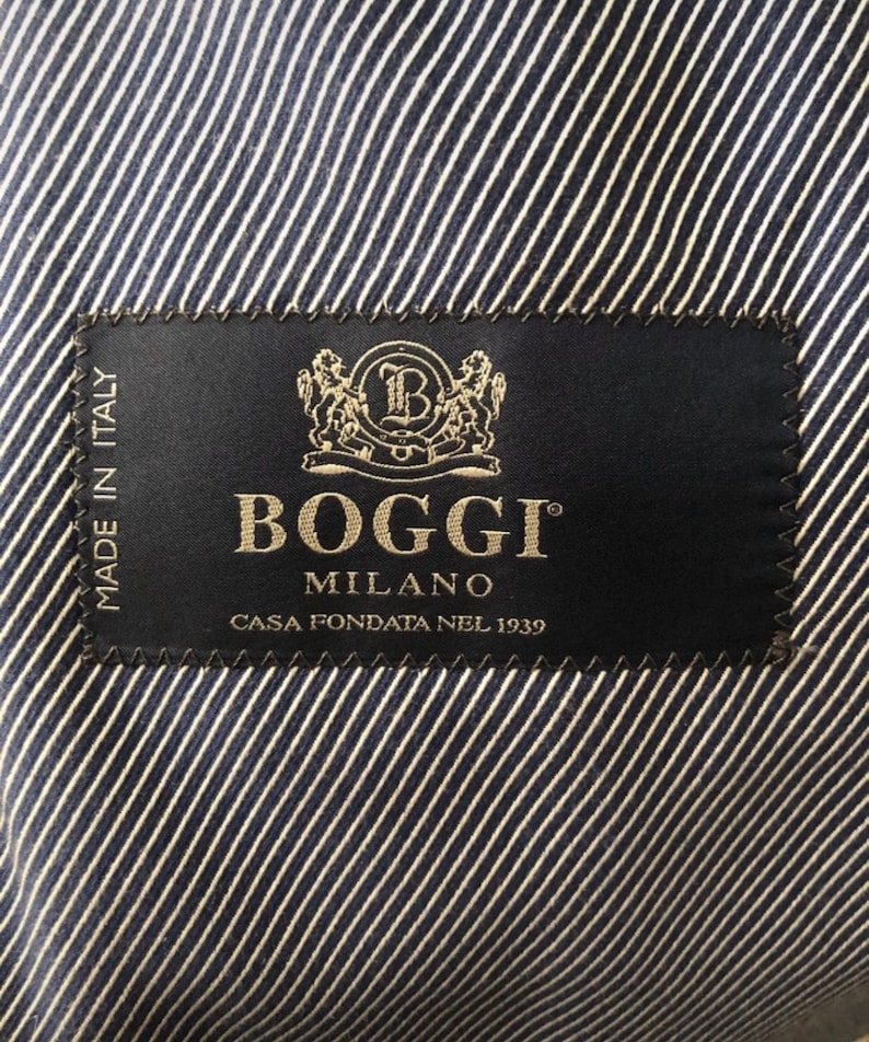 May include: Close-up of a navy blue and white striped fabric with a black label. The label reads "Boggi Milano" in gold lettering, with the text "Casa Fondata Nel 1939" below. The label also says "Made in Italy".