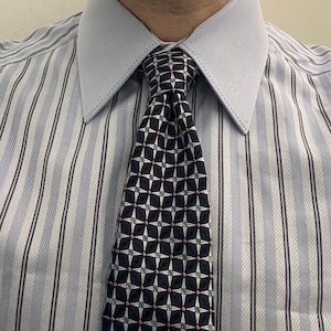 Pu&ograve; includere: Una camicia elegante a righe azzurre e bianche con un colletto azzurro a tinta unita caratterizzato da cuciture decorative lungo i bordi. La camicia &egrave; abbinata a una cravatta blu navy scuro con un motivo geometrico a stella in bianco e rosa.