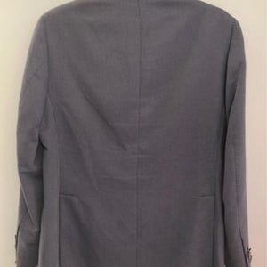 May include: A gray blazer with a subtle, textured pattern. The jacket is hung on a black hanger and features a classic two-button closure, a notched lapel, and a single vent in the back. The fabric appears to be a lightweight material.