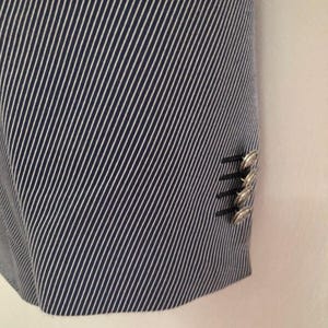 May include: Close-up of a navy blue and white striped blazer. The fabric has a diagonal stripe pattern. The blazer has silver buttons on the sleeve.