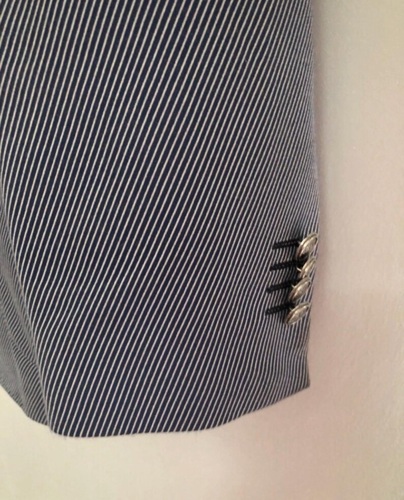 May include: Close-up of a navy blue and white striped blazer. The fabric has a diagonal stripe pattern. The blazer has silver buttons on the sleeve.