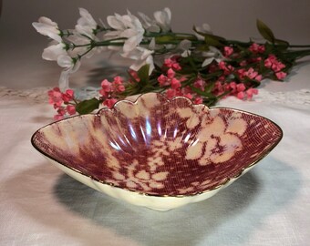May include: A decorative, scalloped-edge dish with a cream-colored exterior and a maroon floral pattern. The interior has an iridescent sheen, and the rim is trimmed with gold. The dish is approximately 8 inches long.