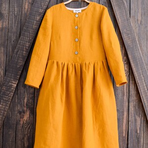 May include: A long-sleeved, mustard yellow linen dress with a button-up front and a gathered skirt.