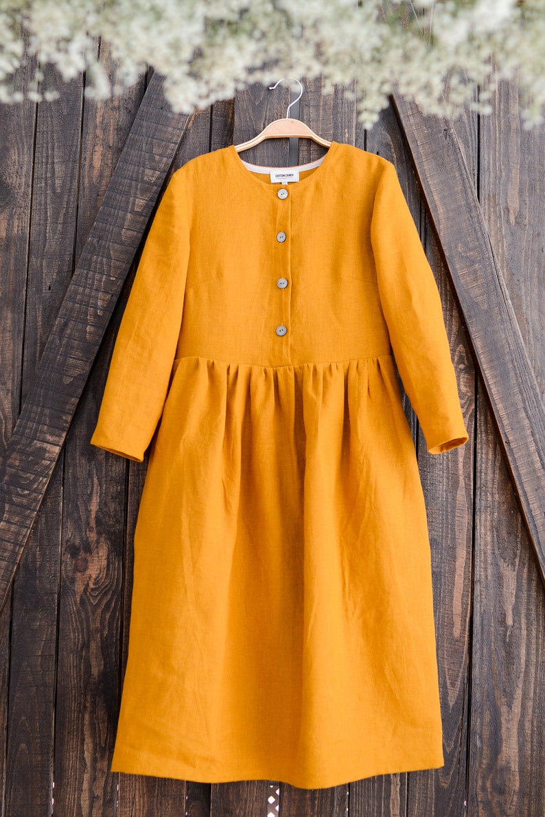 May include: A long-sleeved, mustard yellow linen dress with a button-up front and a gathered skirt.